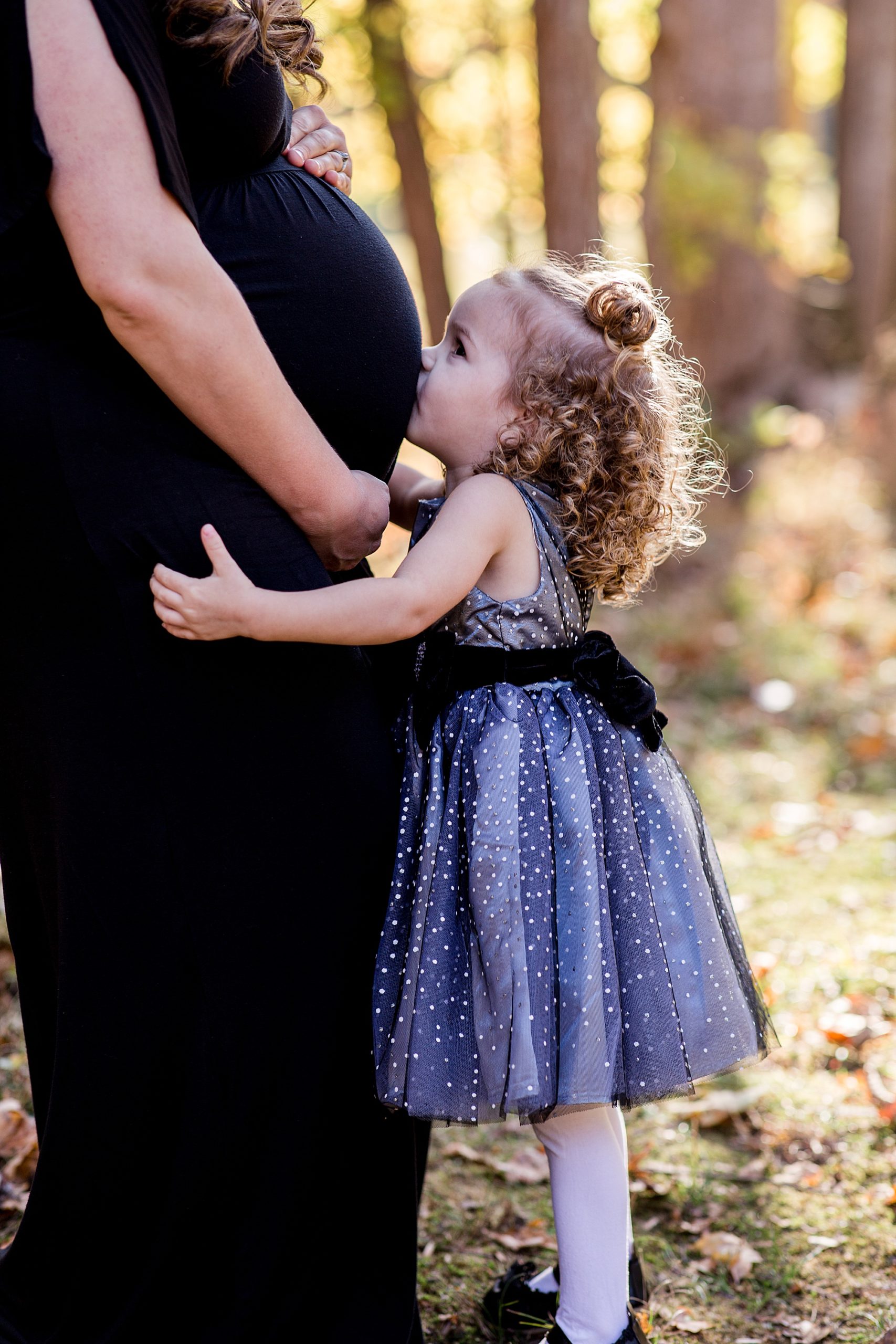 toddler hugs mom and kisses belly during maternity session