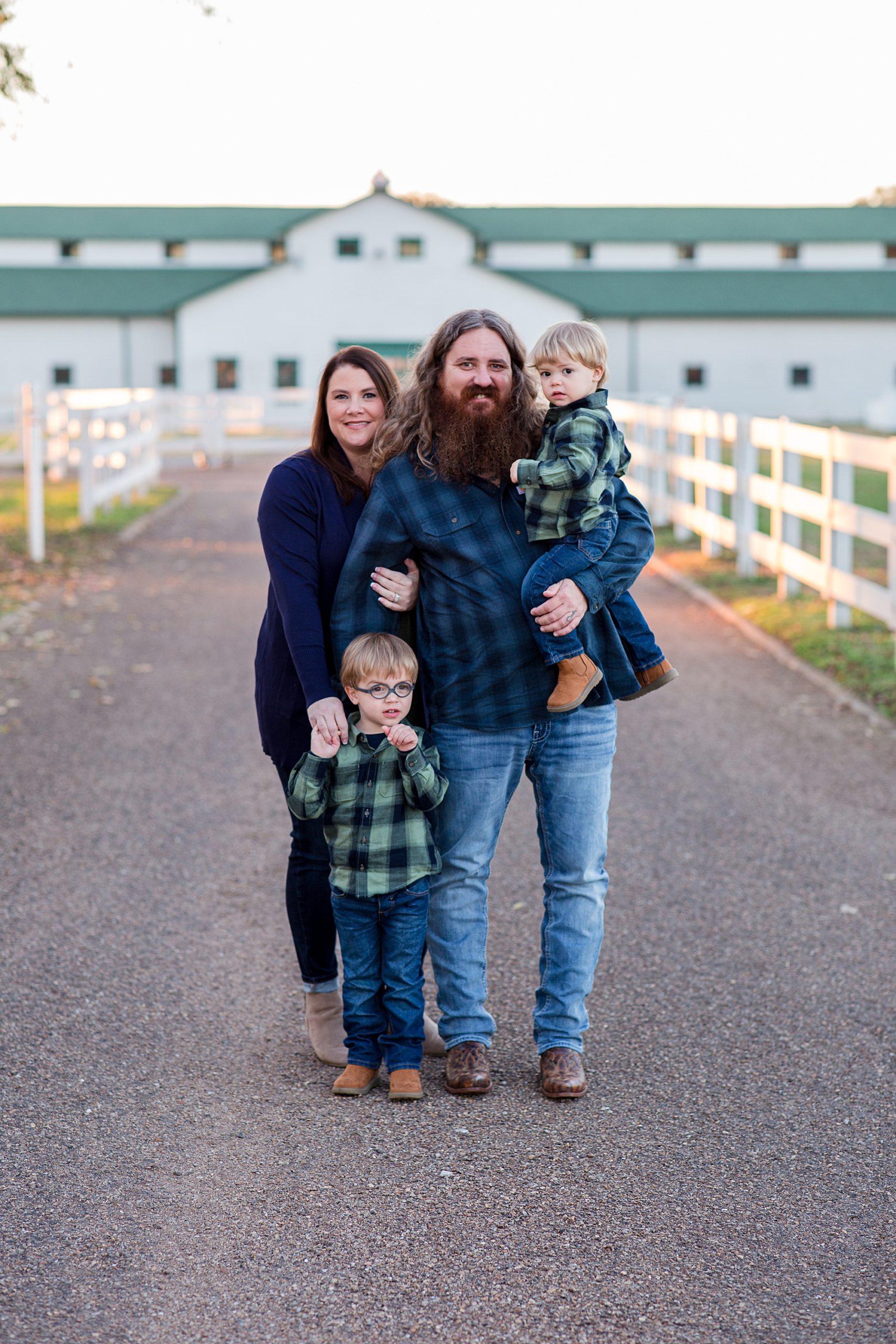 family of four poses outside white barn on driveway during Harlinsdale Farm family portraits