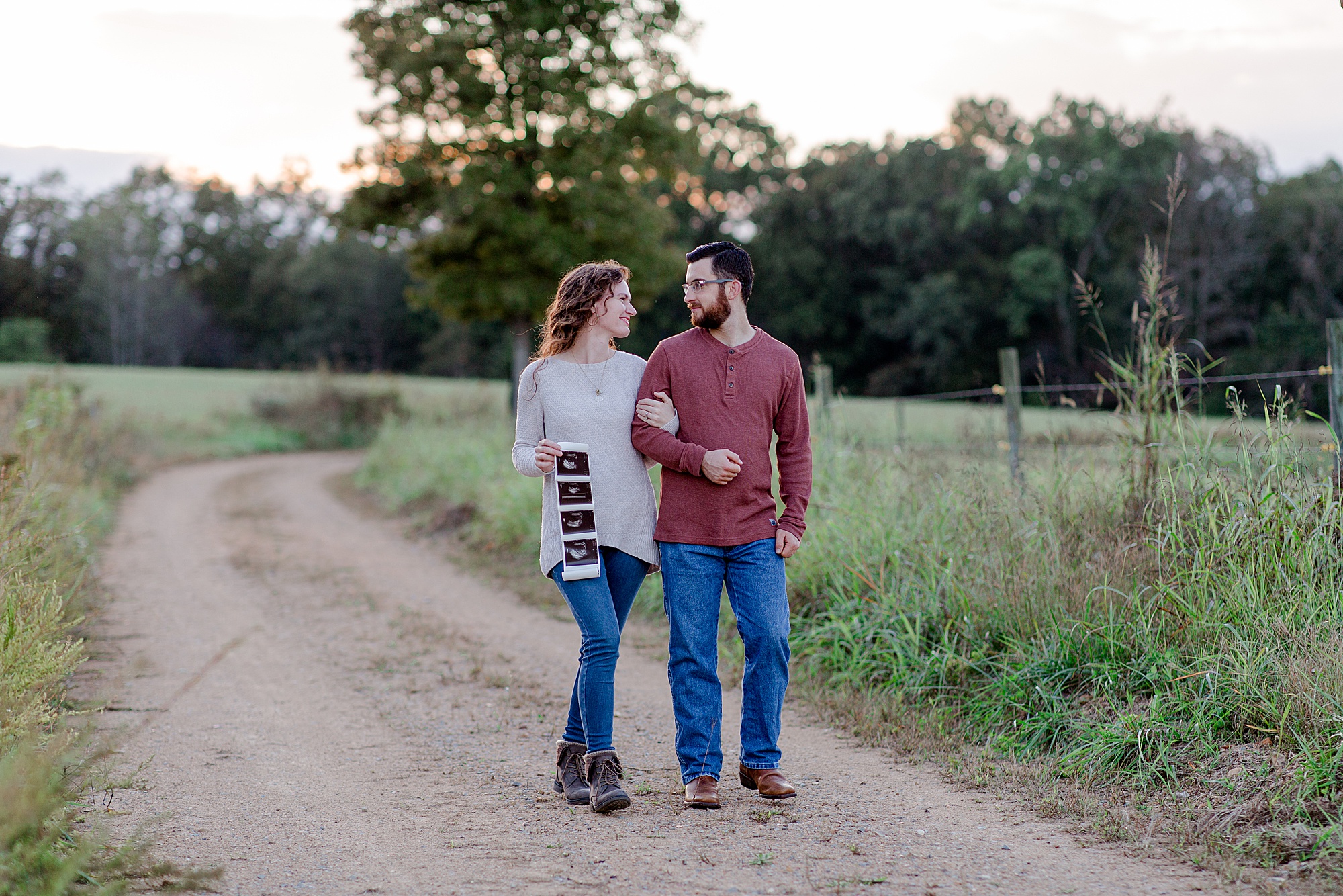 couple walks down dirt road with sonogram