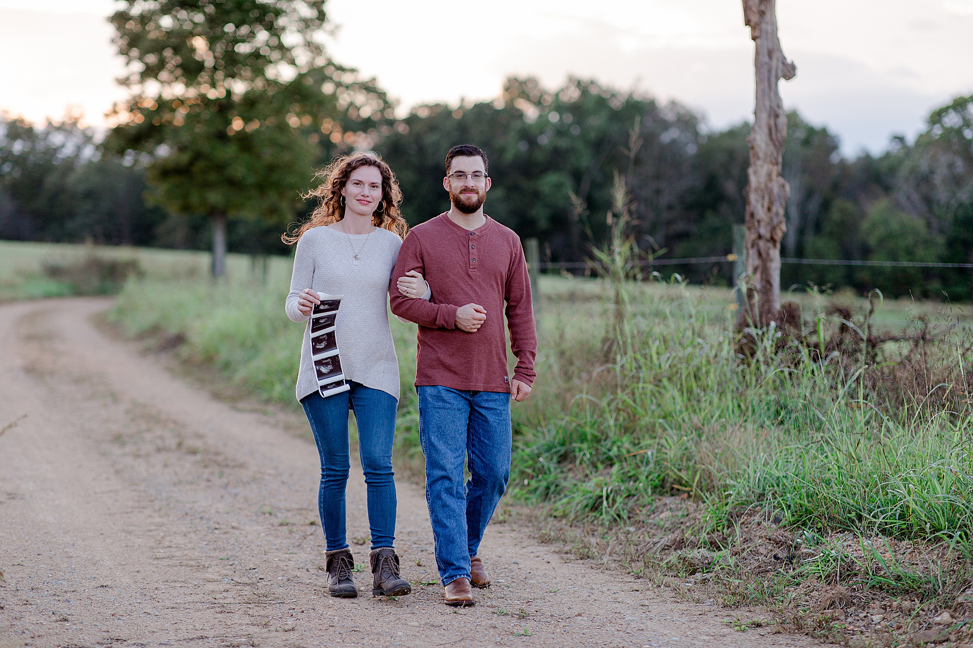 couple walks together showing off sonogram during photos for pregnant announcement 