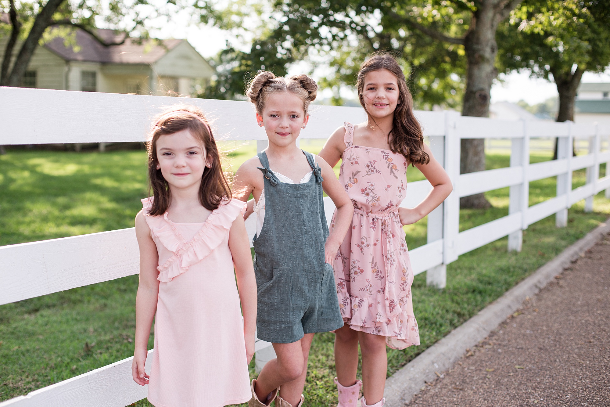 three girls lean on white fence during spring family photos in Tennessee