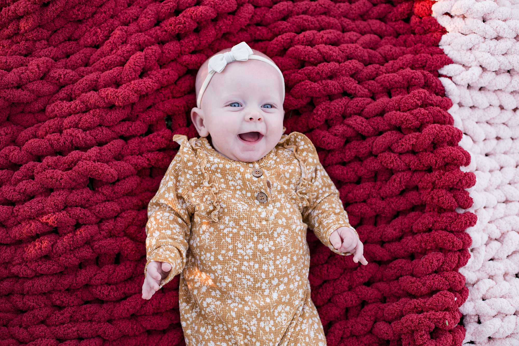 baby in yellow outfit lays on red knit blanket
