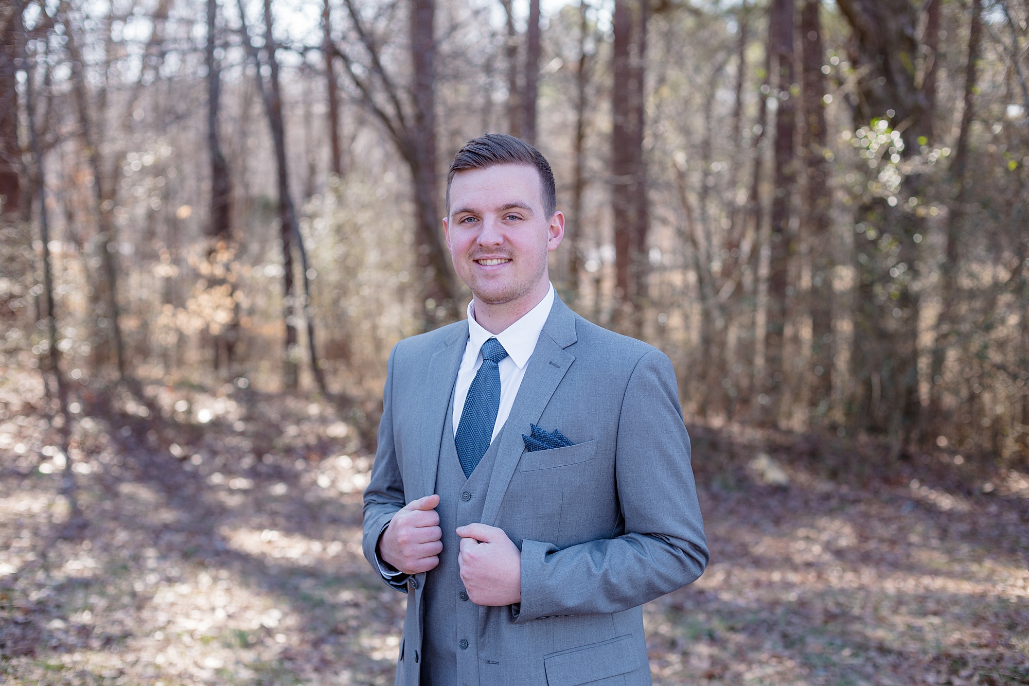 groom poses in grey suit with blue tie